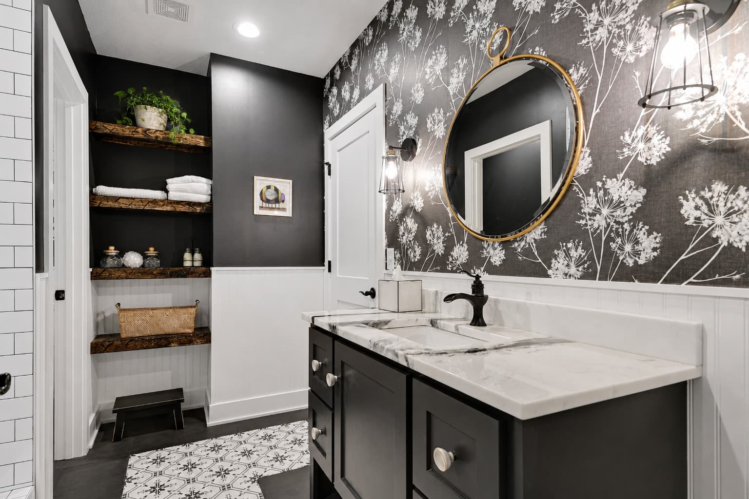 Styled powder bathroom with black floral wallpaper, a brass mirror, floating wood shelves, and a black vanity