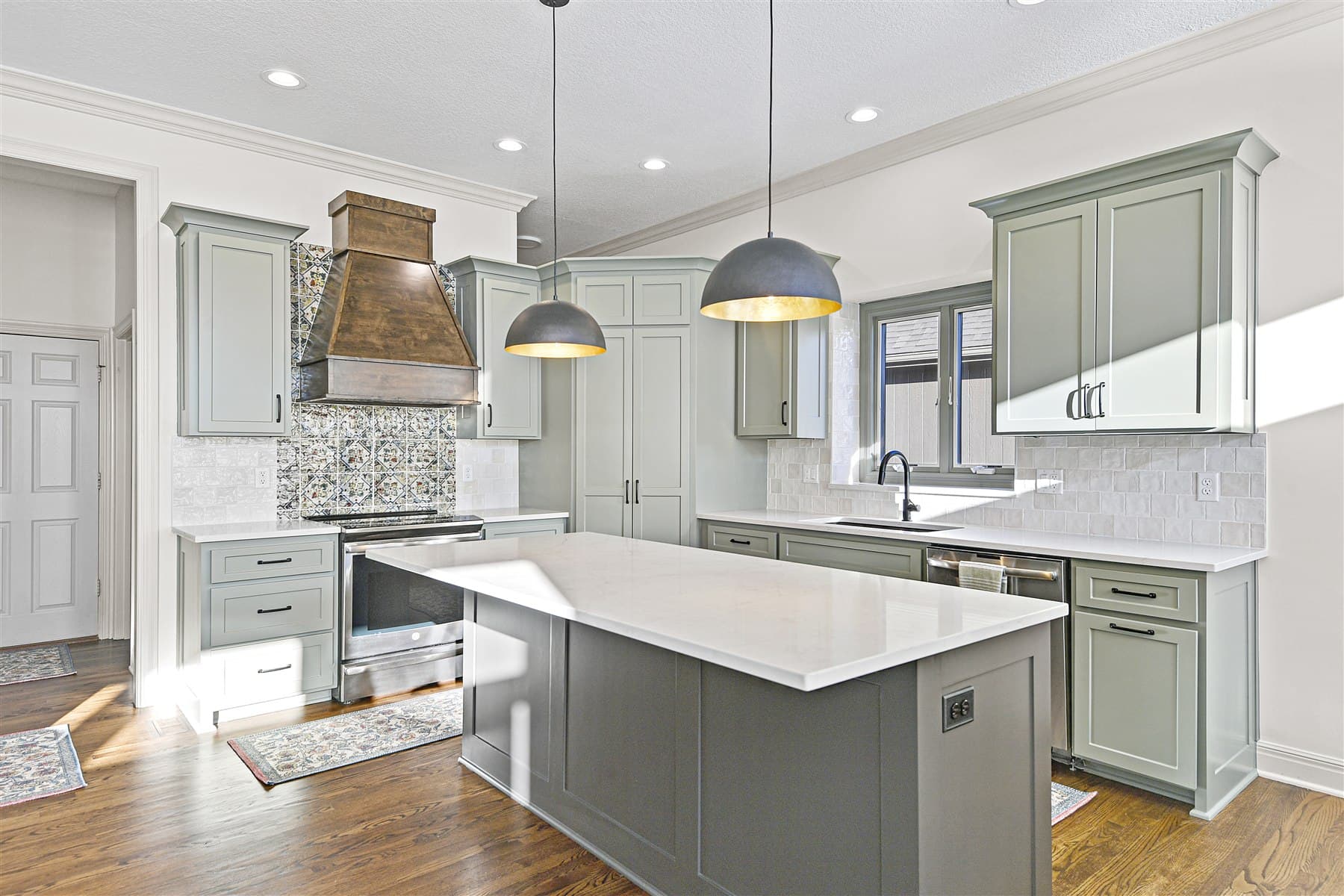 Sage green kitchen with patterned tile and black pendants