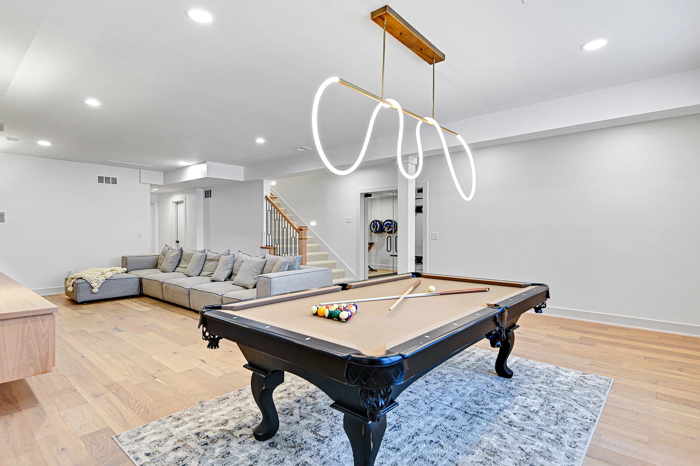 Bright staged entertainment room with a pool table, sectional seating, and sculptural lighting
