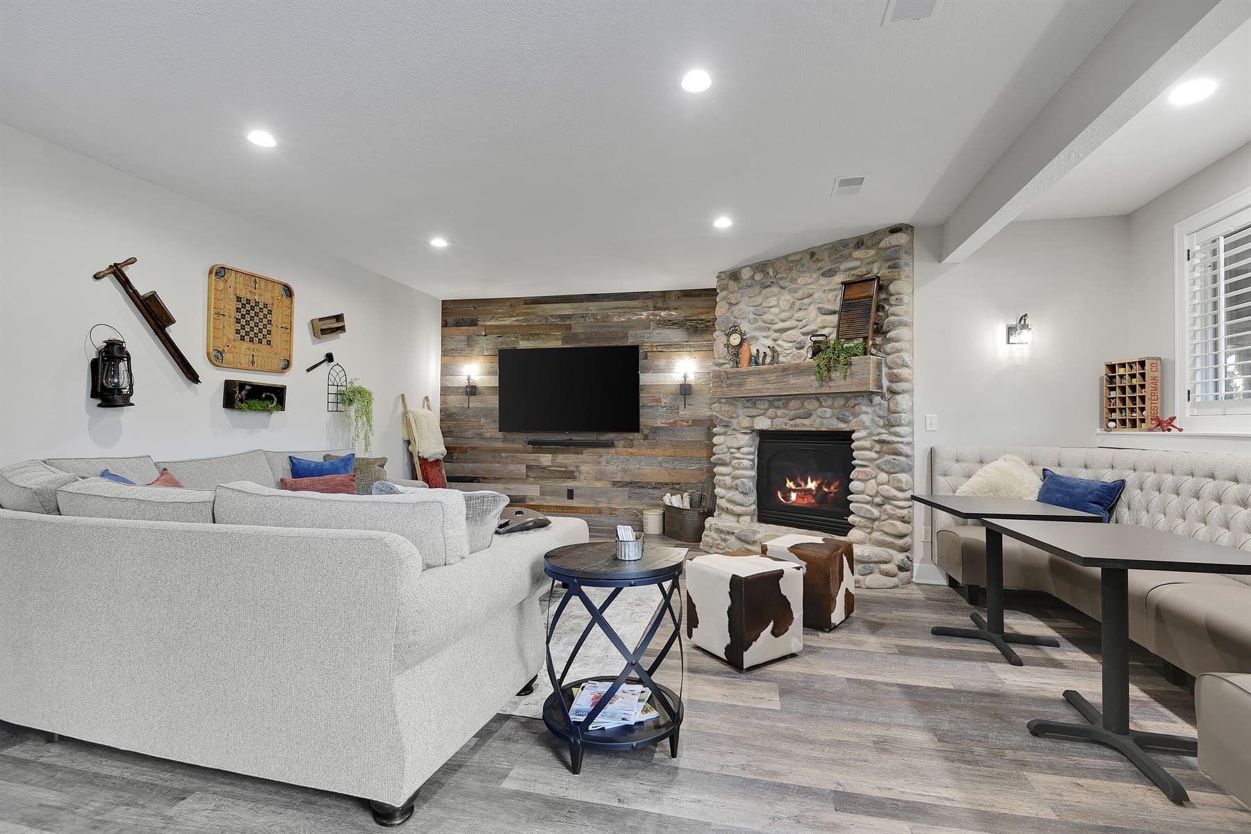 Staged basement lounge with a stone fireplace, layered seating, and rustic wood details