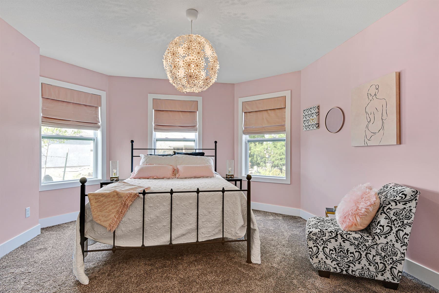 Pink primary bedroom staged with layered bedding, sculptural lighting, and a patterned chair